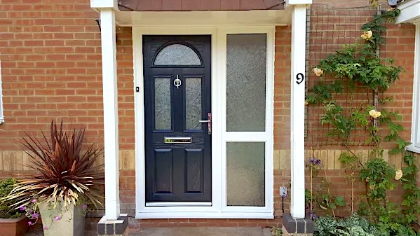 A red brick house surrounded by plants with a New Navy Blue Composite double glazed front door with chrome fittings and a new white upvc side window